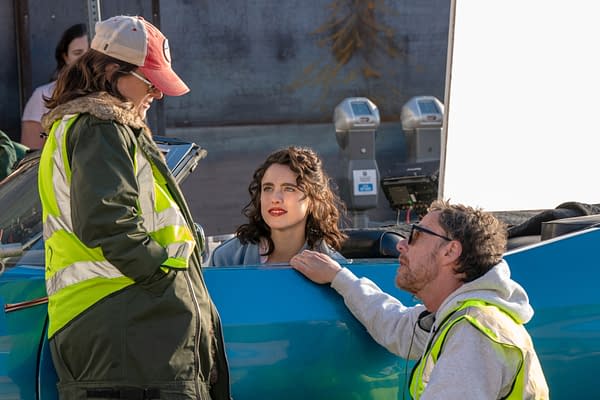 On the set of the film 'HONEY DON'T!', writer Tricia Cooke and writer/director Ethan Coen converse with actor Margaret Qualley, who is seated in a classic convertible car. The crew members are wearing safety vests, indicating a film production environment.
