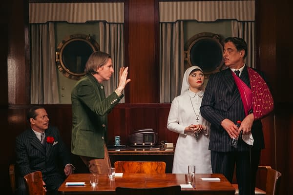 A scene from the film 'THE PHOENICIAN SCHEME', featuring director Wes Anderson and actors Mathieu Amalric, Mia Threapleton, and Benicio Del Toro in a vintage setting with a nautical theme.