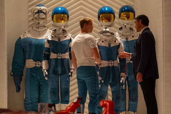 A scene from 'The Fantastic Four: First Steps' featuring two characters, Joseph Quinn as Johnny Storm and Pedro Pascal as Reed Richards, interacting in front of futuristic blue astronaut suits, emphasizing the Sci-Fi theme. The suits prominently display the number '4' symbol.