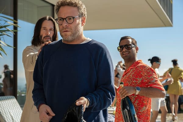 Scene from the movie 'Good Fortune' featuring actors Keanu Reeves as Gabriel, Seth Rogen as Jeff, and Aziz Ansari as Ari. The characters are portrayed in a casual setting, with a party atmosphere in the background.