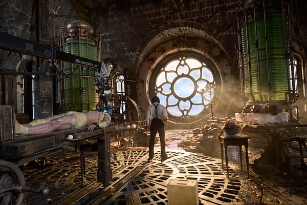 On the set of Frankenstein, Jacob Elordi portrays The Creature while Oscar Isaac as Dr. Victor Frankenstein stands in a dimly lit laboratory with a large stained glass window. The scene features a dramatic atmosphere with scientific equipment and red lighting, emphasizing themes of creation and destruction.