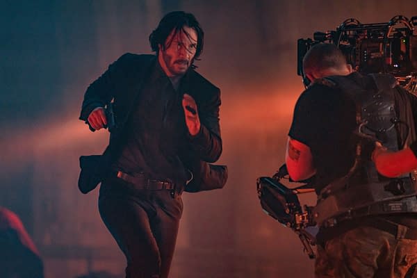 Keanu Reeves as John Wick running in a dramatic scene from John Wick: Chapter 4, with a film camera operator capturing the action in a moody, lit environment.