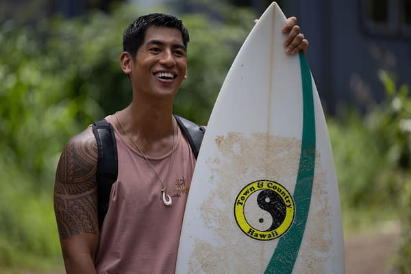 Kaipo Dudoit as David from Disney's live-action 'Lilo & Stitch,' smiling while holding a surfboard, set against a lush green background.