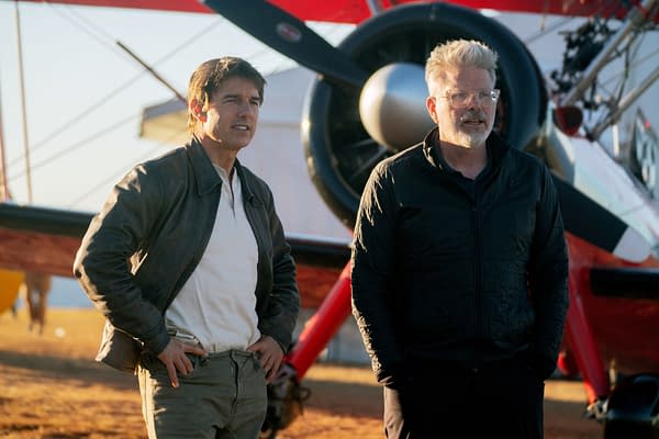 Tom Cruise and Christopher McQuarrie stand on the set of 'Mission: Impossible - The Final Reckoning' in front of a biplane during sunset, with a warm light illuminating the scene.