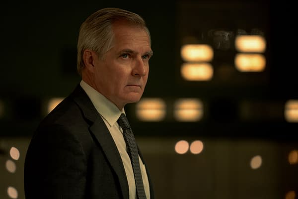 A scene from 'Mission: Impossible - The Final Reckoning' featuring a serious-looking man in a suit, portraying the character Kittridge. The background is dimly lit with blurred lights, creating a tense atmosphere.