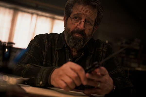 A scene from 'Mission: Impossible - The Final Reckoning' featuring Rolf Saxon as William Donloe, who appears contemplative while holding a pair of scissors in a dimly lit room.