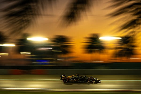 A high-resolution image capturing a Formula 1 car racing along a track at sunset, with blurred palm trees and bright lights in the background, conveying a sense of speed and motion.
