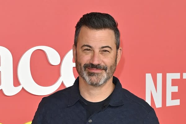 A man with dark hair and a beard smiles warmly against a vibrant red background featuring the word 'Netflix' in white letters. He is wearing a blue collared shirt.