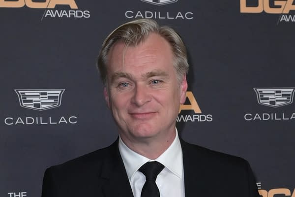A smiling man in a black suit and tie poses in front of a dark backdrop with Cadillac and DGA Awards logos, suggesting a formal event.