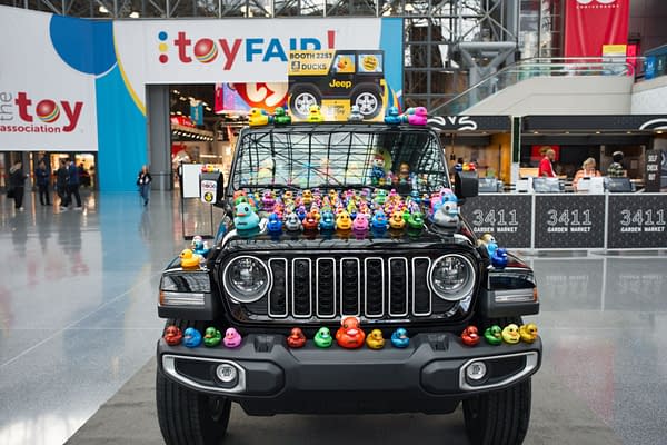 A black Jeep Wrangler decorated with colorful rubber ducks displayed at a toy fair. The background features a vibrant toy fair banner.