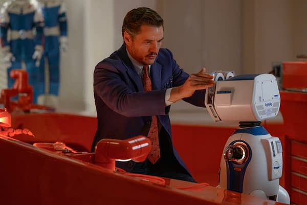 Pedro Pascal portrays Reed Richards/Mister Fantastic in a scene from 'The Fantastic Four: First Steps,' interacting with a futuristic robot in a brightly colored laboratory setting.