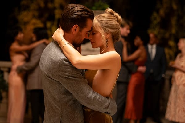 A romantic scene features a couple embracing closely, with their foreheads touching, amidst a softly lit party atmosphere. Guests in elegant attire can be seen dancing in the background.