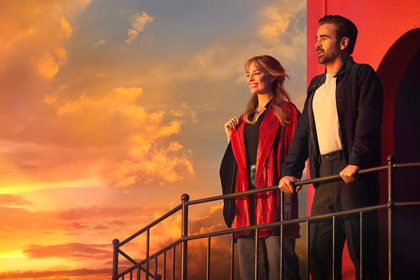 A dramatic scene featuring two characters standing on a balcony, illuminated by a vibrant sunset sky with shades of orange and pink. One character, wearing a red striped coat, smiles, while the other, in dark attire, gazes thoughtfully at the horizon.