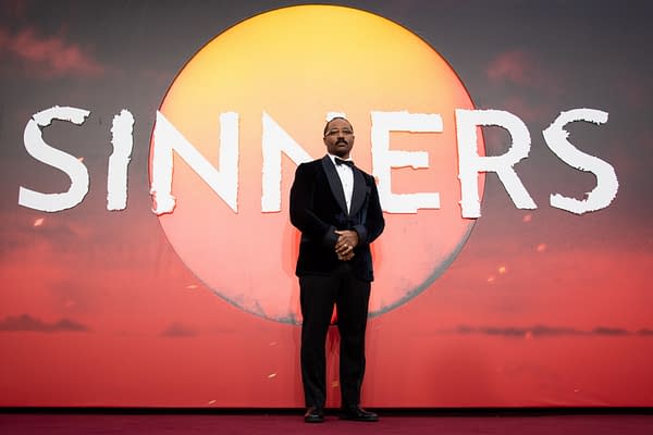 Director Ryan Coogler stands at the European premiere of "Sinners," against a bold backdrop featuring the film's title and a large sun graphic.
