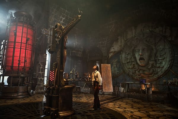 A scene from the film 'Frankenstein,' featuring Oscar Isaac as Victor Frankenstein, gazing up at a large, mechanical assembly in a dark, atmospheric laboratory with a red light and intricate decor.