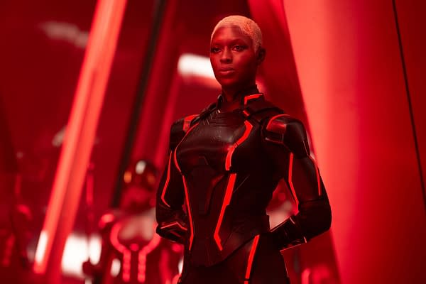 Jodie Turner-Smith as Athena in a sleek, futuristic black suit with glowing red accents, set against a red background in a scene from Disney's live action 'TRON: ARES'.