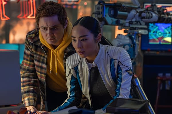 Still from Disney's live-action 'TRON: Ares' featuring Greta Lee as Eve Kim and a male character, both intensely focused on a computer screen, with a brightly lit, futuristic background.