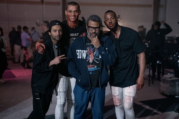 A behind-the-scenes photo from the film 'HIM', featuring director Justin Tipping, producer Jordan Peele, and actors Marlon Wayans and Tyriq Withers, all posing together on set. The scene suggests a mix of sports and horror elements, with some cast members appearing bloodied.