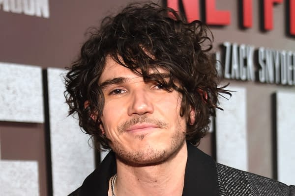 A young man with curly hair and slight facial stubble smiles at the camera, wearing a black jacket. The background features the title 'ZACK SNYDER'S' prominently displayed, indicating its connection to the upcoming film 'The Last Photograph.'