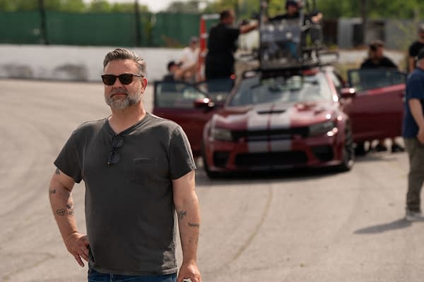 Behind-the-scenes image featuring director Shawn Simmons on the set of 20th Century Studios' 'EENIE MEANIE,' with a red car and crew in the background.