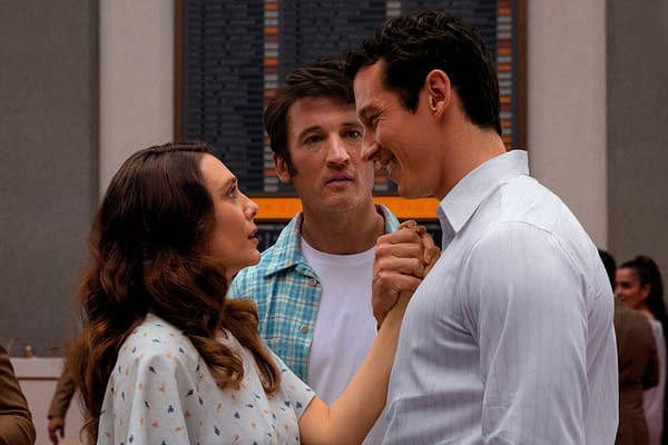A tense scene featuring three characters: a woman in a hospital gown looking worriedly at a man in a white shirt, who is smiling as he holds her hand; a man in a plaid shirt stands between them, appearing concerned. The background suggests a clinical setting.
