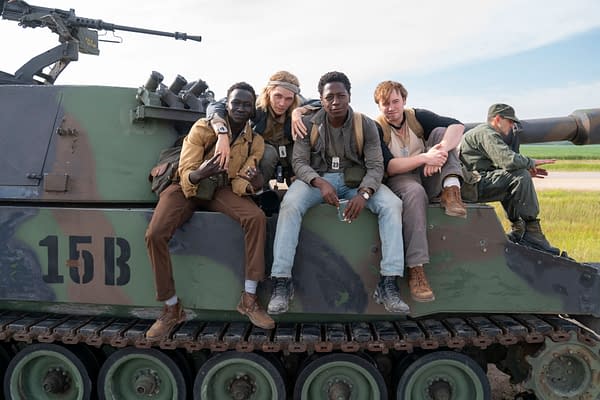 A group of four young men and one man in military attire sit on a tank, engaging with each other in a relaxed pose. The scene is from 'The Long Walk,' depicting camaraderie among the characters.