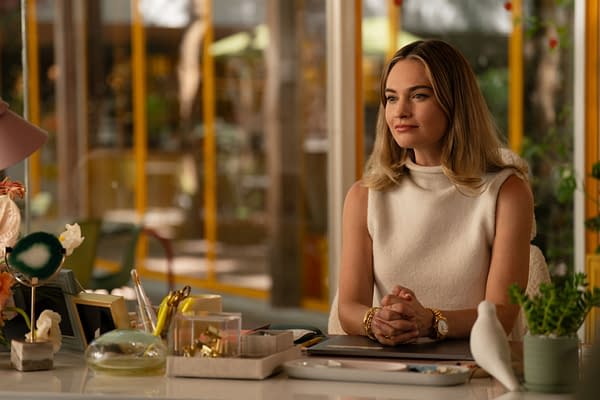 Lily James portrays Whitney Wolfe Herd in a scene from 20th Century Studios' 'Swiped', seated at a desk adorned with stationery and decor, featuring a light, modern aesthetic with greenery in the background.