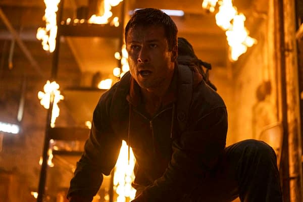 Glen Powell appears as a character in a scene from the Paramount Pictures film "The Running Man," with flames and smoke in the background, conveying a dramatic and intense moment.
