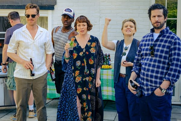 A group of five actors, including Benedict Cumberbatch and Kate McKinnon, appear at a social gathering, smiling and holding drinks. They are dressed casually, with a picnic table in the background displaying food and beverages.