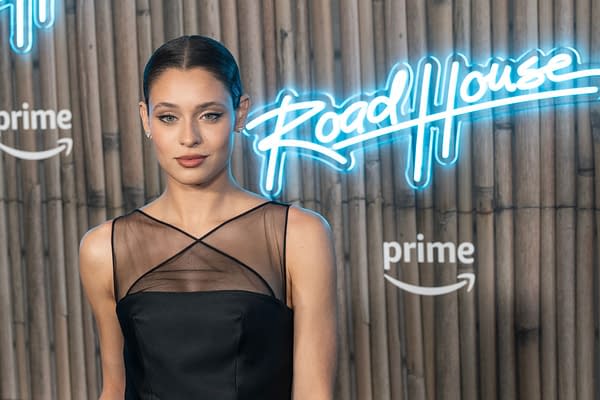 Daniela Melchior poses at the premiere of 'Road House' wearing a chic black Prada dress, with a neon 'Road House' sign and Amazon Prime logo in the background.