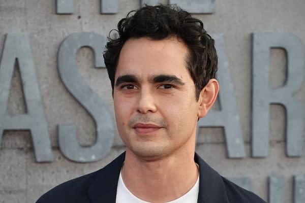 Max Minghella, an actor known for his work in 'The Handmaid's Tale,' appears at a premiere event in Los Angeles, dressed in a navy blazer and white shirt, with a neutral expression against a textured backdrop.