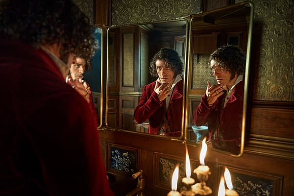 Oscar Isaac as Victor Frankenstein gazes into a mirror in a dimly lit room, reflecting a moment of contemplation. The scene features ornate wooden decor and candlelight, enhancing the gothic atmosphere.