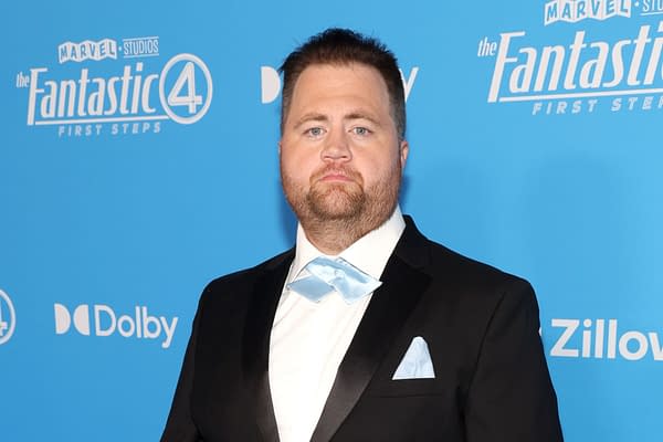 A man in a formal black tuxedo with a light blue bow tie and pocket square poses against a blue backdrop featuring the logo for 'The Fantastic 4.'