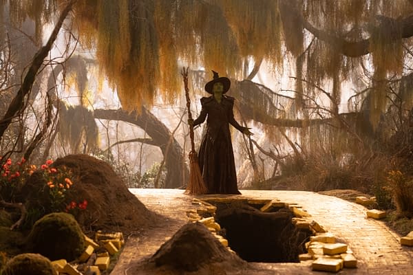 A scene from 'Wicked: For Good' featuring Cynthia Erivo as Elphaba, standing on a golden brick path in a mystical forest with overhanging moss and trees, holding a broomstick.