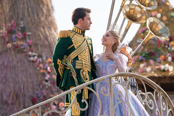 In a scene from 'WICKED FOR GOOD,' Jonathan Bailey as Fiyero stands on a decorative bridge with Ariana Grande as Glinda, who wears a sparkling gown and tiara, both smiling at each other amidst a vibrant floral backdrop.