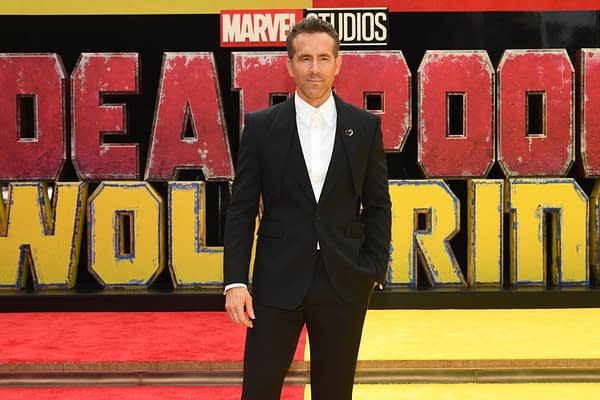 Ryan Reynolds poses on the red carpet at the Deadpool & Wolverine World Premiere in New York City, with large, colorful promotional signage in the background.