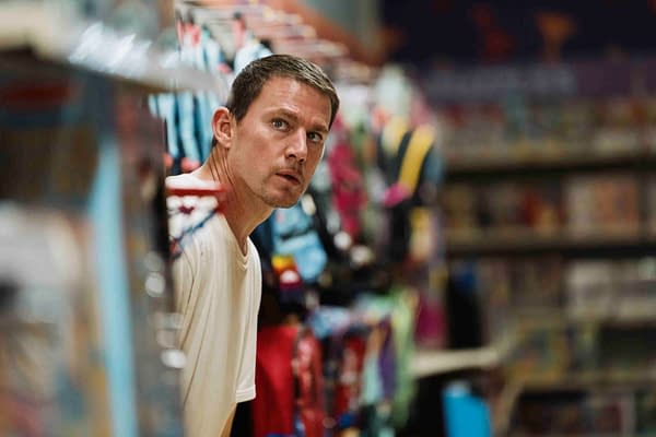 A tense scene featuring Channing Tatum as he peeks around a rack of colorful clothing and costume items, hinting at a moment of surprise or intrigue.
