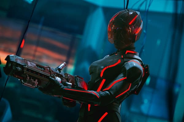 Jodie Turner-Smith as Athena in a futuristic suit with glowing red accents, holding a weapon, set against a high-tech background in a scene from Disney's Live Action TRON: ARES.