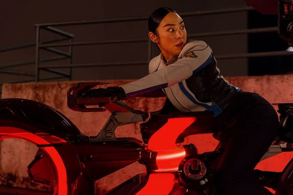 Greta Lee as Eve Kim in Disney's Live Action TRON: ARES, depicted on a futuristic vehicle with glowing red accents, showcasing an intense expression in a dynamic pose.