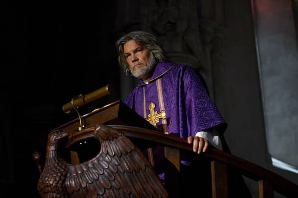 A dramatic scene from "Wake Up Dead Man: A Knives Out Mystery" featuring a man with long, gray hair and a beard, dressed in a richly decorated purple robe with a cross insignia, standing by a wooden lectern adorned with an eagle design. The lighting is moody, emphasizing the intensity of the moment.