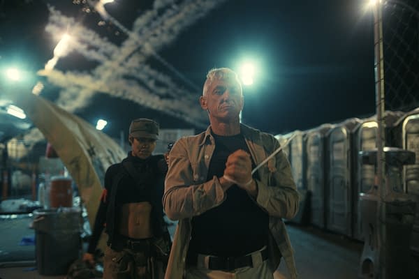 A dramatic scene featuring a man with white hair and a serious expression, appearing to be restrained. He is flanked by a woman in a military-style outfit, with a confident stance while holding a weapon. The background shows a chaotic nighttime scene with smoke trails and portable restrooms.