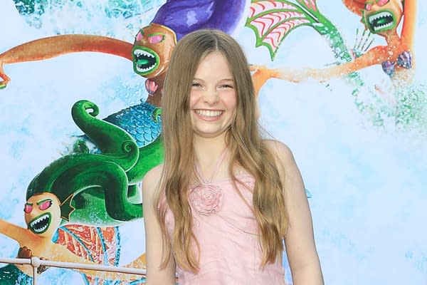 A smiling girl with long hair, wearing a pink dress, stands in front of a colorful background featuring animated characters from 'The Angry Birds 3' movie, including a mermaid and other whimsical figures.