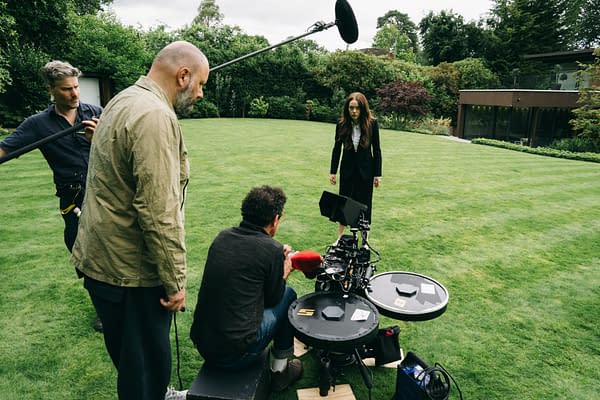 Director Yorgos Lanthimos, director of photography Robbie Ryan, and actress Emma Stone are on the set of the film 'BUGONIA' in a lush green garden, with filming equipment visible.