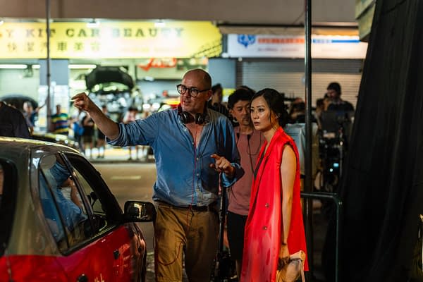 Ballad of a Small Player A scene from the film 'Ballad of a Small Player' shows a director guiding an actress in a vibrant red outfit, while crew members are visible in a bustling urban setting.