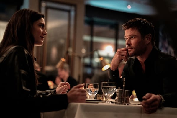 Maya (Monica Barbaro) and Davis (Chris Hemsworth) engaged in a conversation at a dinner table, showcasing a tense yet intimate moment in a restaurant setting from the film 'Crime 101.'