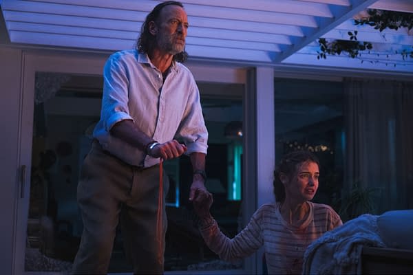 A tense scene from the film 'Primate' features Troy Kotsur as Adam and Gia Hunter as Erin, with Adam gripping a string tightly while Erin appears distressed, her face showing signs of injury. The lighting is moody, creating a dramatic atmosphere.
