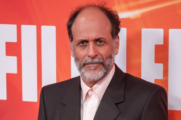 A man with a beard and thin hair, wearing a dark suit, poses in front of a vibrant orange background with the word 'FILM' prominently displayed. He has a serious expression, suggesting an event or interview setting.