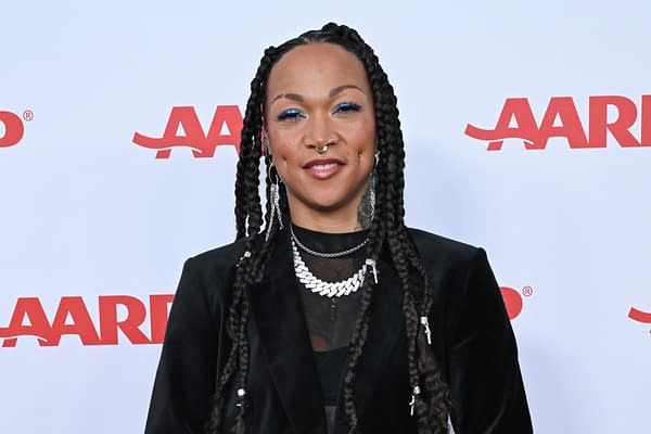 A woman with long, braided hair wearing a black outfit and silver jewelry stands in front of an AARP backdrop, smiling confidently.