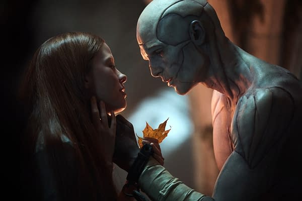 Mia Goth as Elizabeth gently touches Jacob Elordi as The Creature in a poignant moment from 'Frankenstein.' The Creature holds a dried leaf, highlighting a connection between the characters.