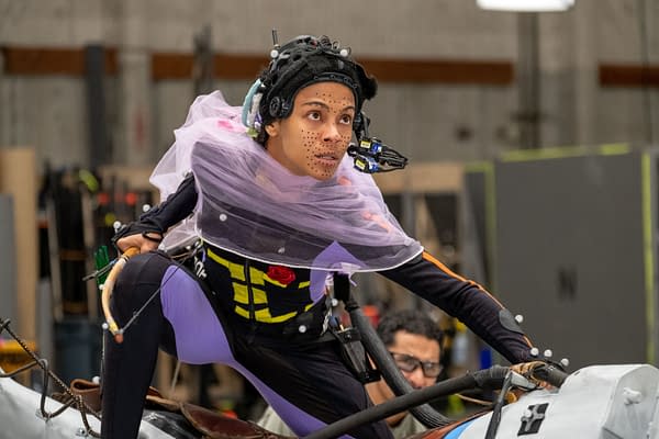 Zoe Saldaña performs in a motion capture suit on the set of 'Avatar: Fire and Ash', with sensor equipment attached to her head and a bow in her hand, displaying a focused expression.